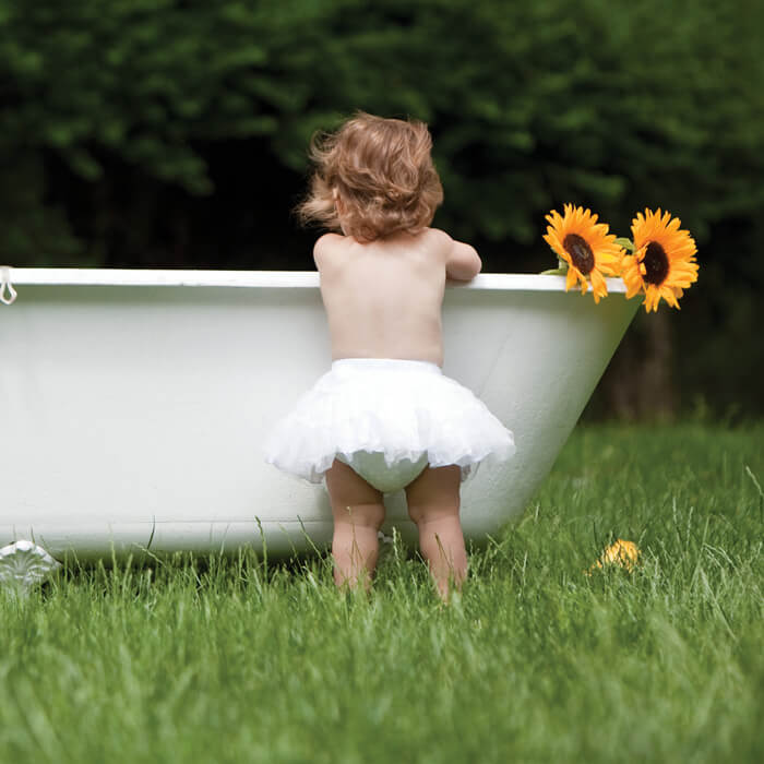 A little girl standing near bath tub on a green grass.